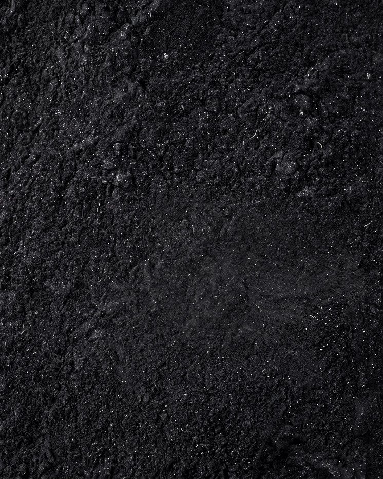 Fine black charcoal powder, closely packed, with small lumps, shallow hollows and scattered grains catching the light.